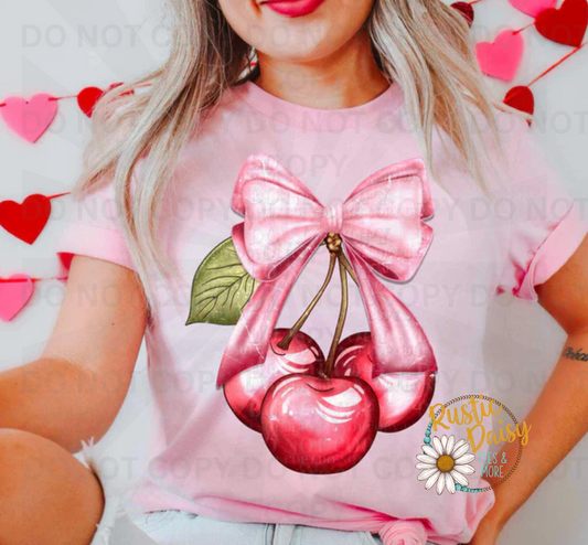 Three red cherries with green stems and pink ribbon bow